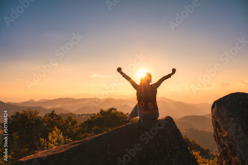 Young hiker woman relaxing and enjoying the sunset view on top of mountain peak at national park photo