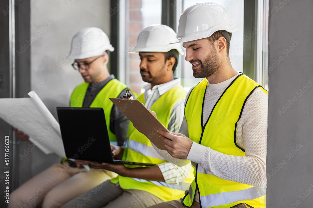 architecture, construction business and people concept - group of male architects in helmets with laptop, blueprint and clipboard working at office architecture, construction business and people concept - group of male architects in helmets with laptop, blueprint and clipboard working at office