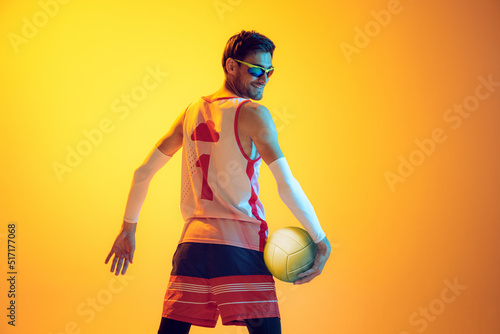 Portrait of young man, beach volleyball player posing isolated over yellow studio background in neon light.