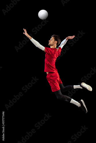 Portrait of young man, volleyball player in motion, training, playing isolated over black studio background. Active