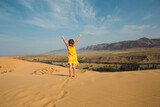 A tourist girl in a yellow dress runs along a sandy dune in the desert. Travel, sights of Dagestan, Sarykum dune
