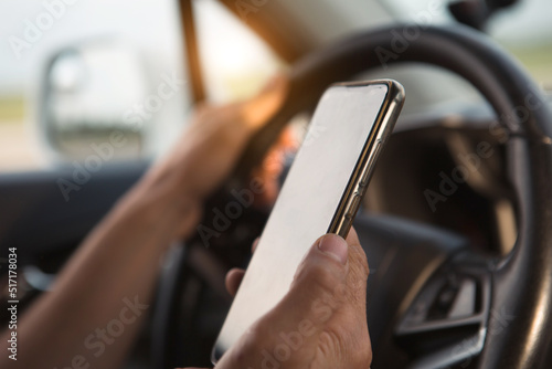 The driver's hand behind the wheel holds a smartphone. Navigator, satellite navigation, communication in the car, road safety, speakerphone