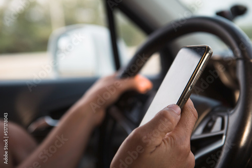 The driver's hand behind the wheel holds a smartphone. Navigator, satellite navigation, communication in the car, road safety, speakerphone