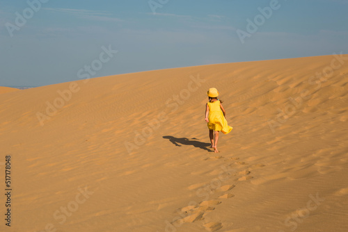 A tourist girl in a yellow dress runs along a sandy dune in the desert. Travel, sights of Dagestan, Sarykum dune