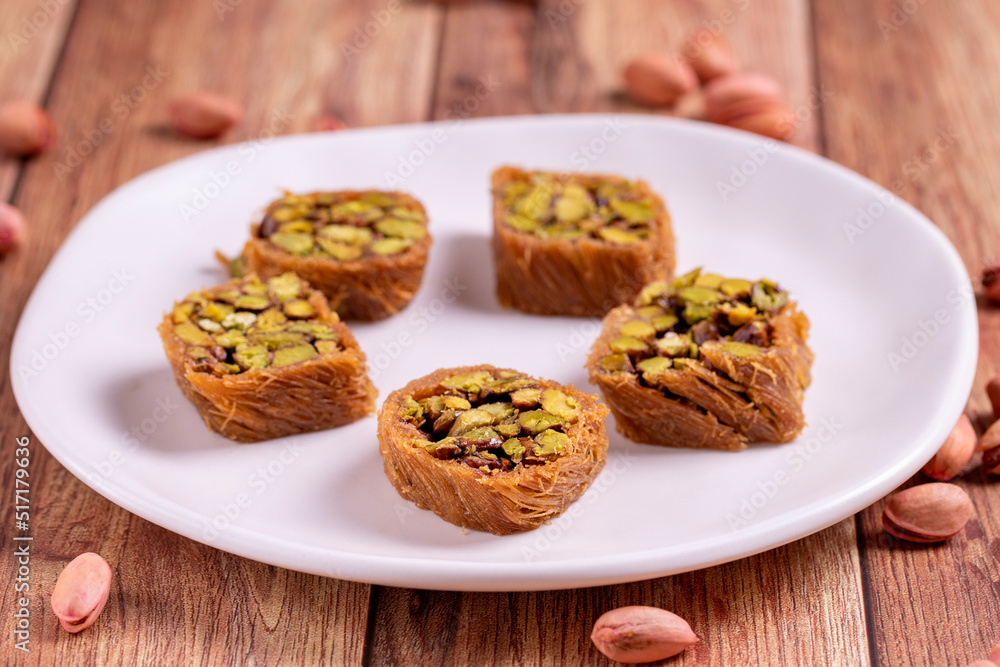 Pistachio kadayif dessert. Kadayif baklava with pistachio filling on a wooden floor. Turkish cuisine desserts. Close-up. local name fıstıklı kadayif Pistachio kadayif dessert. Kadayif baklava with pistachio filling on a wooden floor. Turkish cuisine desserts. Close-up. local name fıstıklı kadayif