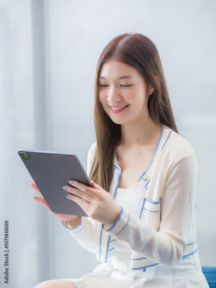 Professional young age Asian business woman with long hair in white shirt holds tablet her smiling happily while she sits on chair in workplace office. Professional young age Asian business woman with long hair in white shirt holds tablet her smiling happily while she sits on chair in workplace office.