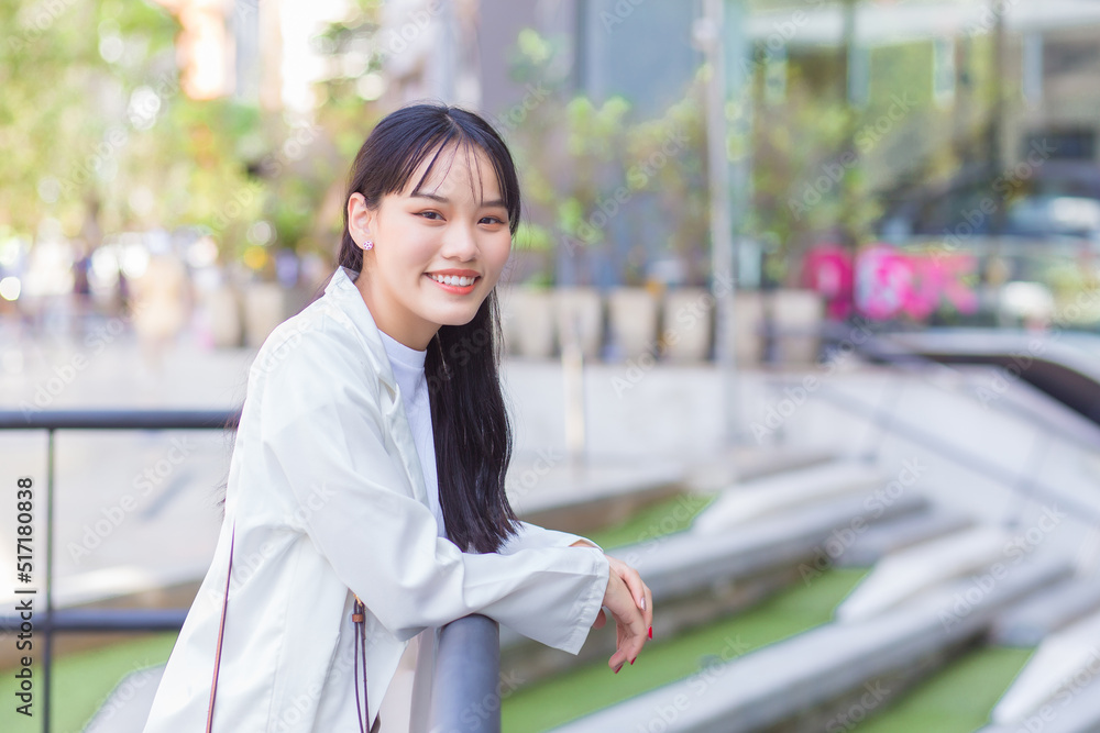 Confident young business Asian working female who wears a white shirt and shoulder bag smiles happily while she is standing on the way to the office for work in the city. Confident young business Asian working female who wears a white shirt and shoulder bag smiles happily while she is standing on the way to the office for work in the city.