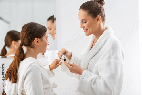 beauty, hygiene, morning and people concept - happy smiling mother and daughter applying toothpaste to toothbrush at bathroom