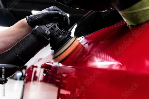 Employee of a car wash or a car detailing studio polishes the car paint with an electric polisher photo