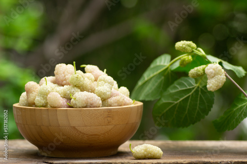 Fresh white mulberries in bowl on wooden table in the garden, summer fruit concept 