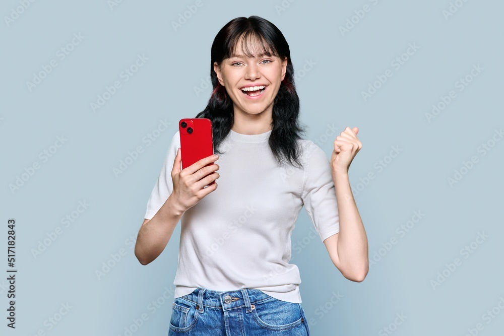 Portrait of happy girl with smartphone raising her fist up, yes symbol Portrait of happy girl with smartphone raising her fist up, yes symbol