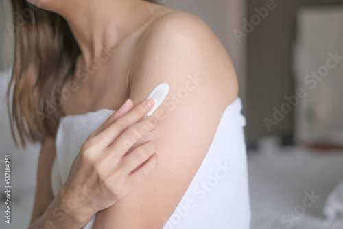 Asia woman sitting on bed and applying cream on her arm.