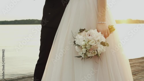 Bride holding a bouquet by the lake during sunset photo