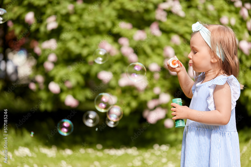 childhood, leisure and people concept - little girl blowing soap bubbles at summer park or garden