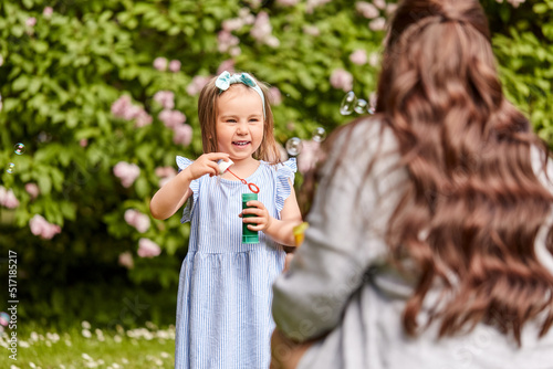 family, motherhood and people concept - happy mother with little daughter blowing soap bubbles at summer park or garden