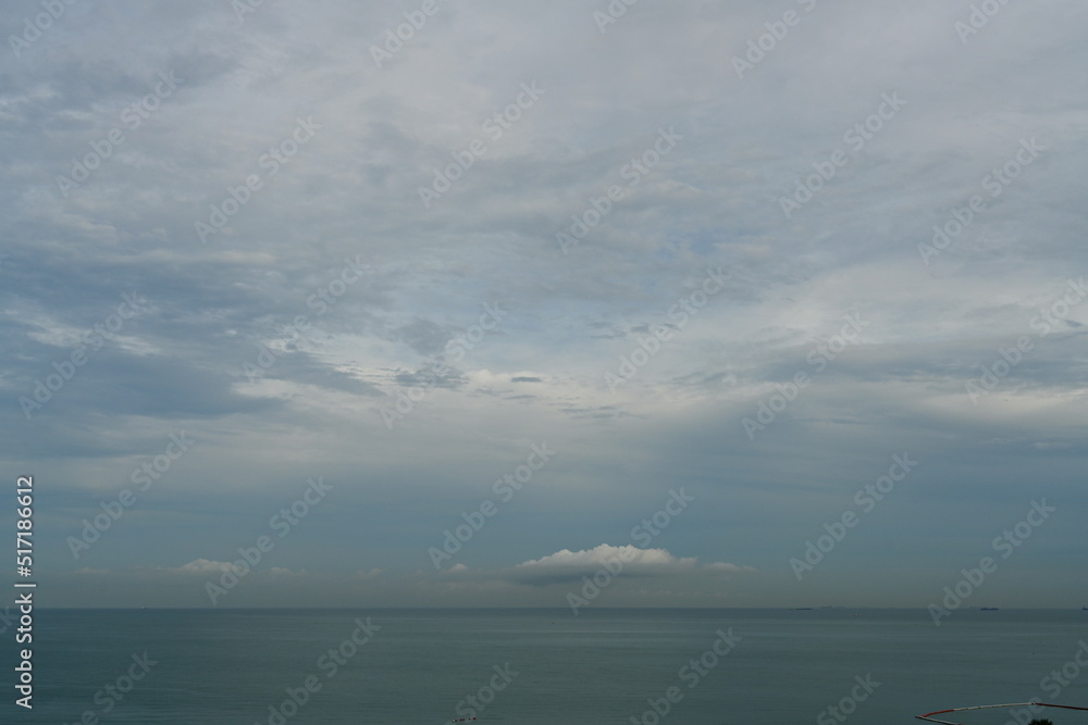 The evening atmosphere of the sea has few waves. Scattered clouds, no sunlight, calm sea, light gray clouds in the rainy season.
