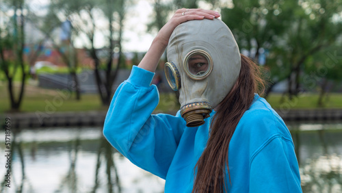 Girl with long hair in a gas mask on the river bank. Alienation in the city. Fashion, ecology and loneliness concepts.
