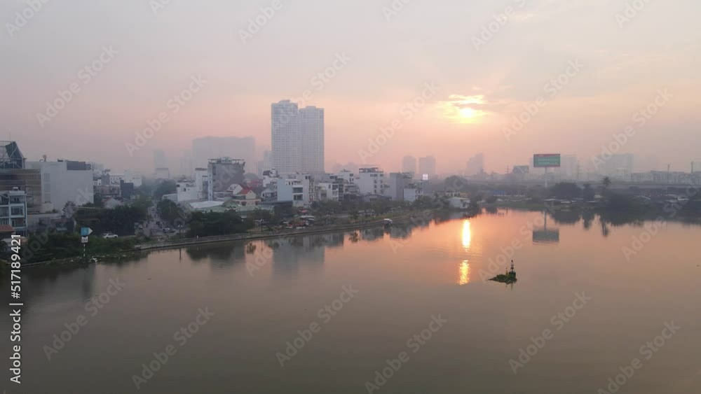 Aerial view of the sun reflecting from calm river water, misty sunrise in Ho Chi Minh City, Vietnam - low, reverse, drone shot Aerial view of the sun reflecting from calm river water, misty sunrise in Ho Chi Minh City, Vietnam - low, reverse, drone shot