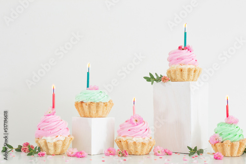 pink and green cupcakes with spring flowers  on wooden podiums on white  back...