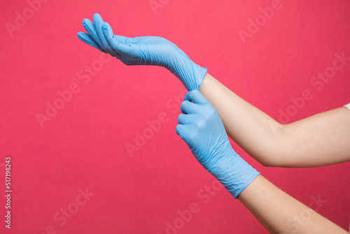 Two hands of a woman wearing nitrile gloves on a pink background