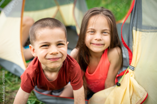 Two little adorable kids smiling and looking out of tent in camp in forest in summer outdoors