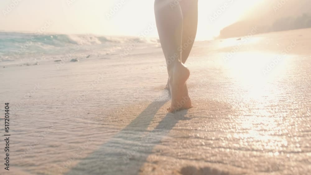 Woman bare feet taking steps on wet sand washed by waters of ocean waves, girl does not want to leave beach and goes towards sun setting over hills relaxing after hard working week at summer resort