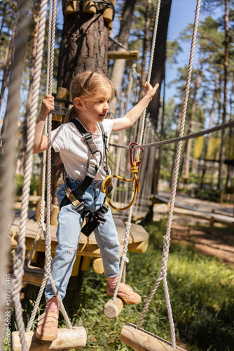 Happy child, school girl enjoying activity in a climbing adventure park on a summer day.