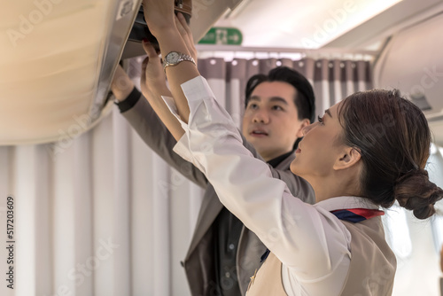 Businessman putting suitcase in overhead compartment with female flight attendant helping, Airline business