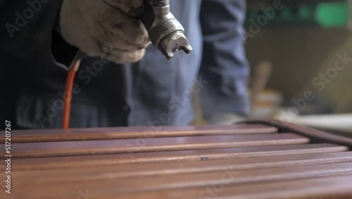 Slow motion. Carpenter-men wearing gloves, apply varnish or primer with compressed air on a wooden surface. Painting of wooden products with a spray gun in a carpentry workshop at a furniture factory