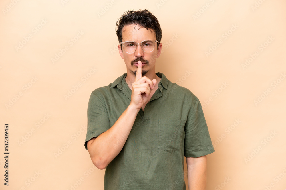 Young caucasian man isolated on beige background showing a sign of silence gesture putting finger in mouth Young caucasian man isolated on beige background showing a sign of silence gesture putting finger in mouth