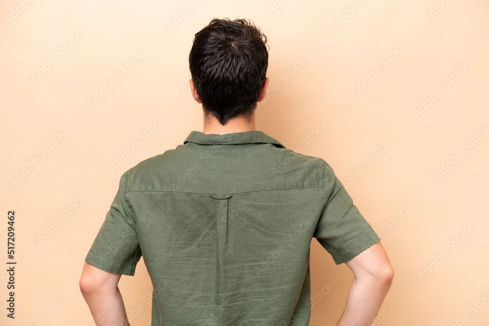 Young caucasian man isolated on beige background in back position Young caucasian man isolated on beige background in back position