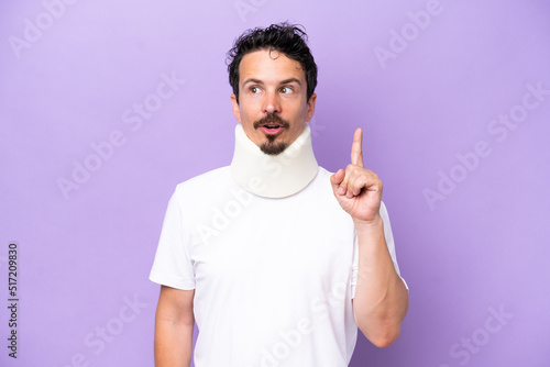 Young caucasian man wearing neck brace isolated on purple background thinking an idea pointing the finger up