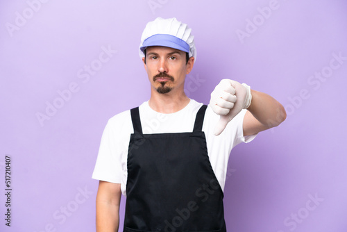Fishmonger man wearing an apron isolated on purple background showing thumb down with negative expression