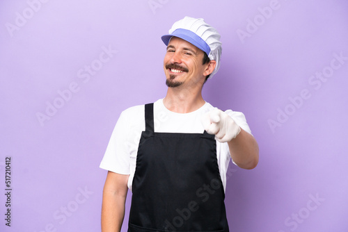 Fishmonger man wearing an apron isolated on purple background pointing front with happy expression