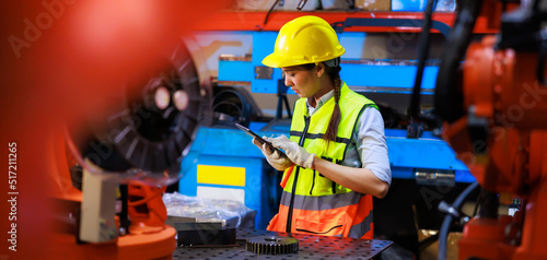 Female industrial factory engineer and technician worker wearing safety vest and hard hat helmet use laptop computer working. Metal lathe industrial manufacturing factory. Opertor automation robot
