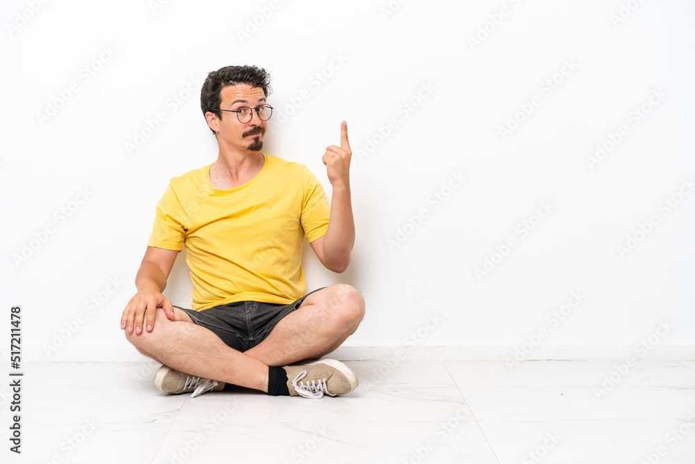 Young caucasian man sitting on the floor isolated on white background pointing with the index finger a great idea