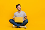 Full length photo of boss brunet millennial guy sit with laptop look promo wear t-shirt jeans shoes isolated on yellow background