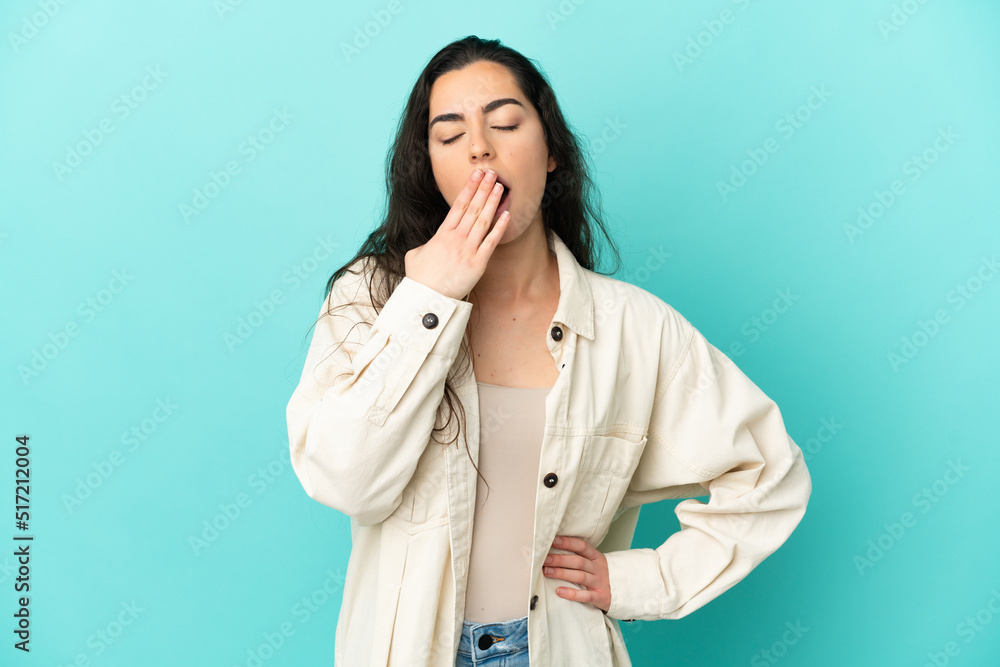 Young caucasian woman isolated on blue background yawning and covering wide open mouth with hand Young caucasian woman isolated on blue background yawning and covering wide open mouth with hand