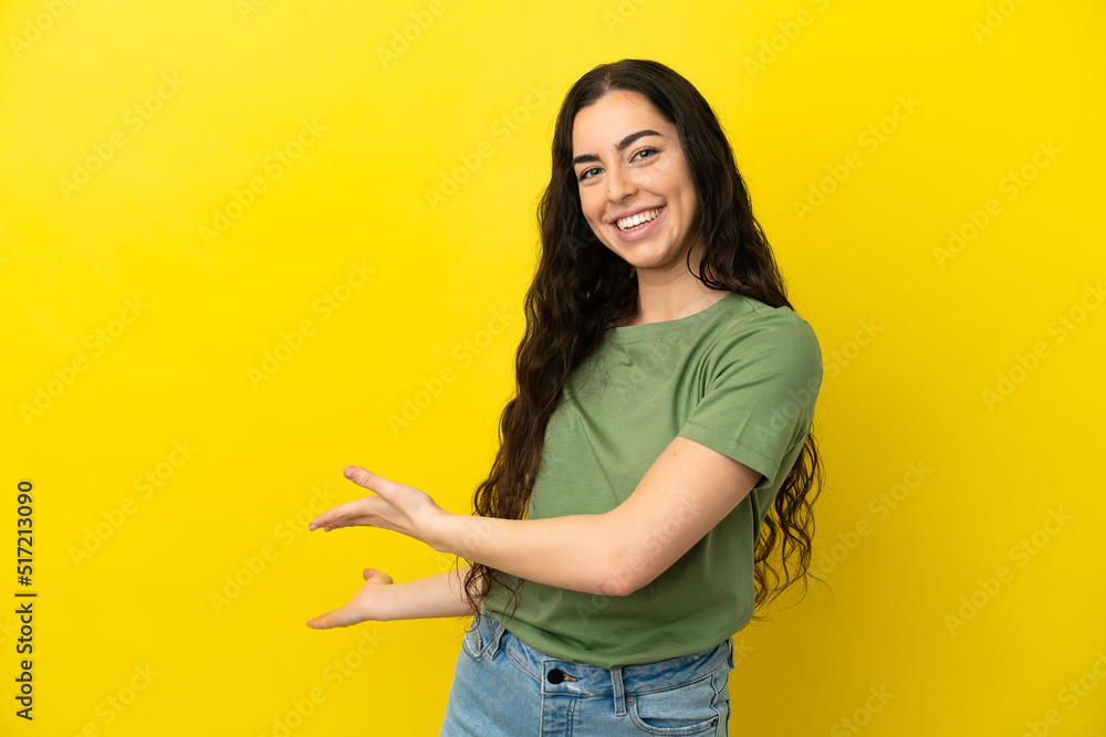 Young caucasian woman isolated on yellow background extending hands to the side for inviting to come Young caucasian woman isolated on yellow background extending hands to the side for inviting to come