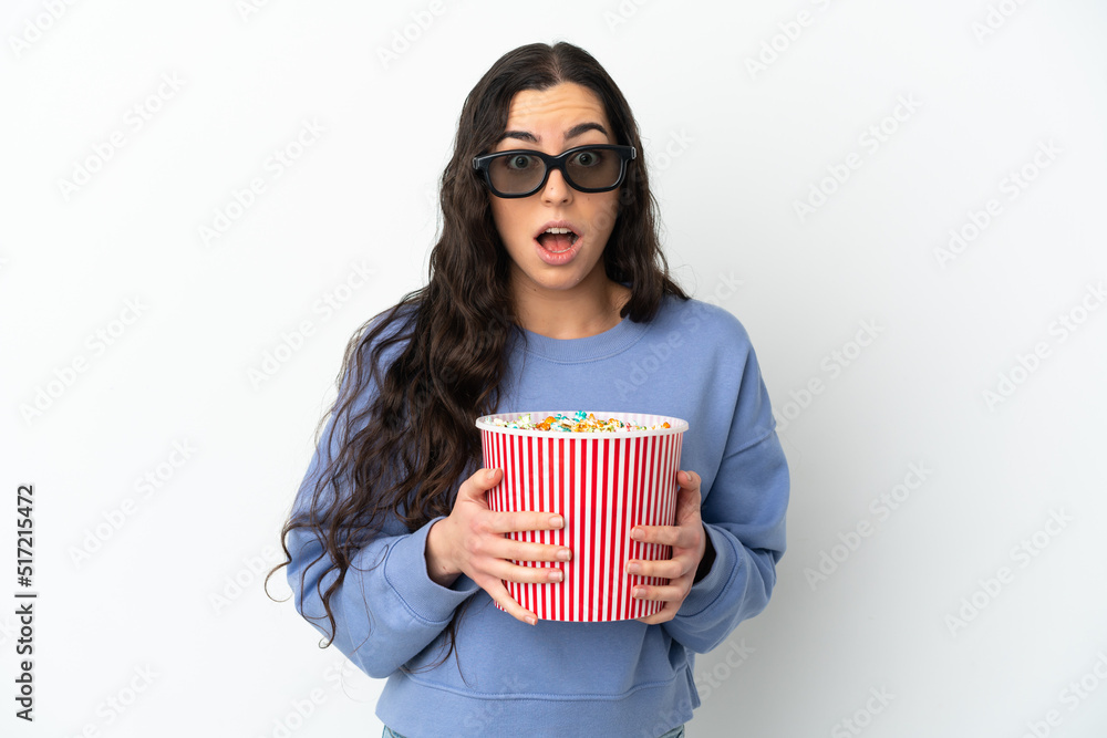 Young caucasian woman isolated on white background surprised with 3d glasses and holding a big bucket of popcorns Young caucasian woman isolated on white background surprised with 3d glasses and holding a big bucket of popcorns