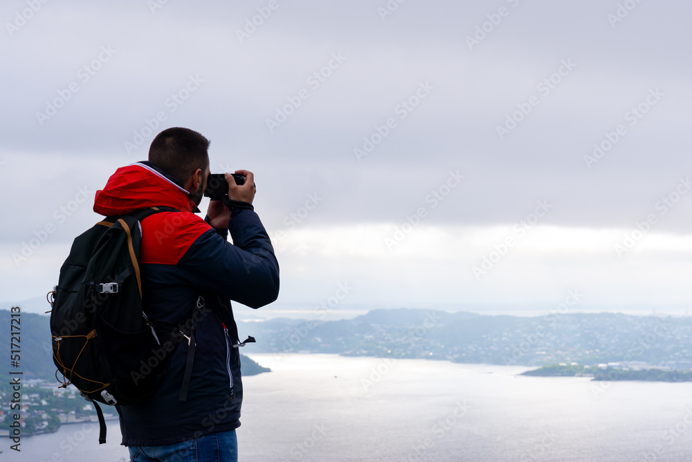 Unrecognizable young man with his backpack on his back and photographing the city of Bergen and the fjord in Norway.