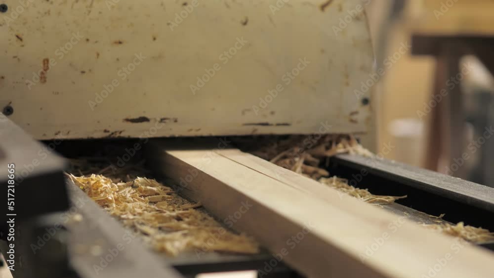 A carpenter in the workshop works on a woodworking machine, processes and aligns wood for the manufacture of furniture parts. The board comes out after processing, a large amount of sawdust