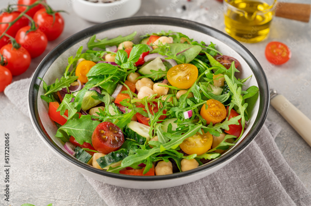 Salad with chickpeas, green leaves and fresh vegetables in a bowl on a gray concrete background. Healthy food. Top view, copy space.