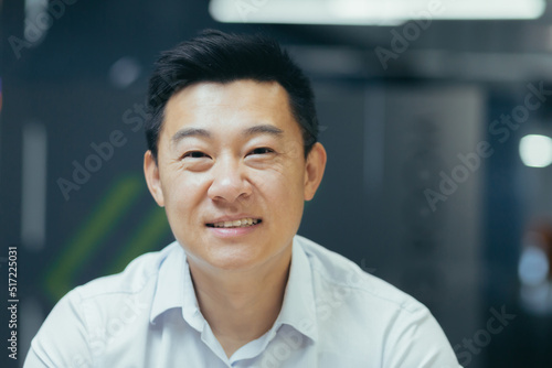 Close-up photo. Portrait of young handsome smiling Asian businessman in white shirt in modern office