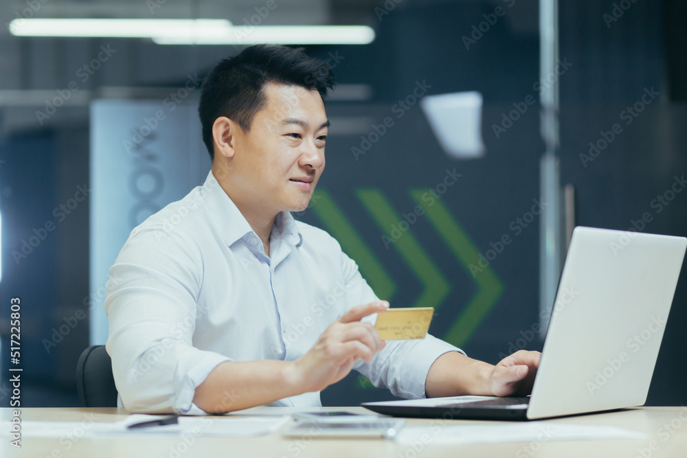 Young handsome male Asian businessman working with laptop and doing credit card transactions. holding in hand, typing. Sitting in the office at the desk Young handsome male Asian businessman working with laptop and doing credit card transactions. holding in hand, typing. Sitting in the office at the desk