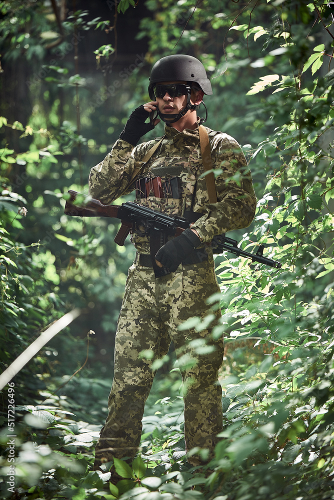 Ukrainian army soldier in uniform and helmet talking on the phone in the forest