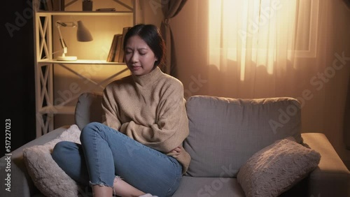 Pms cramps. Menstrual pain. Female period symptom. Disturbed unwell woman suffering from belly ache on couch in modern home interior.