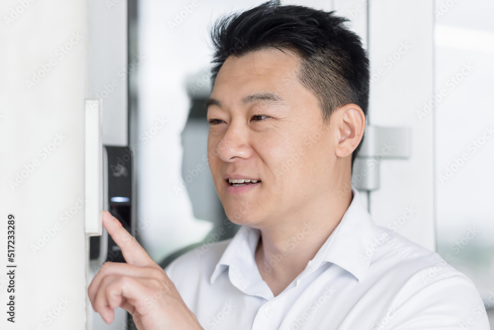 Close-up photo. Portrait of a young handsome Asian man, calling the intercom of the house, pressing the button, waiting for the door to open.