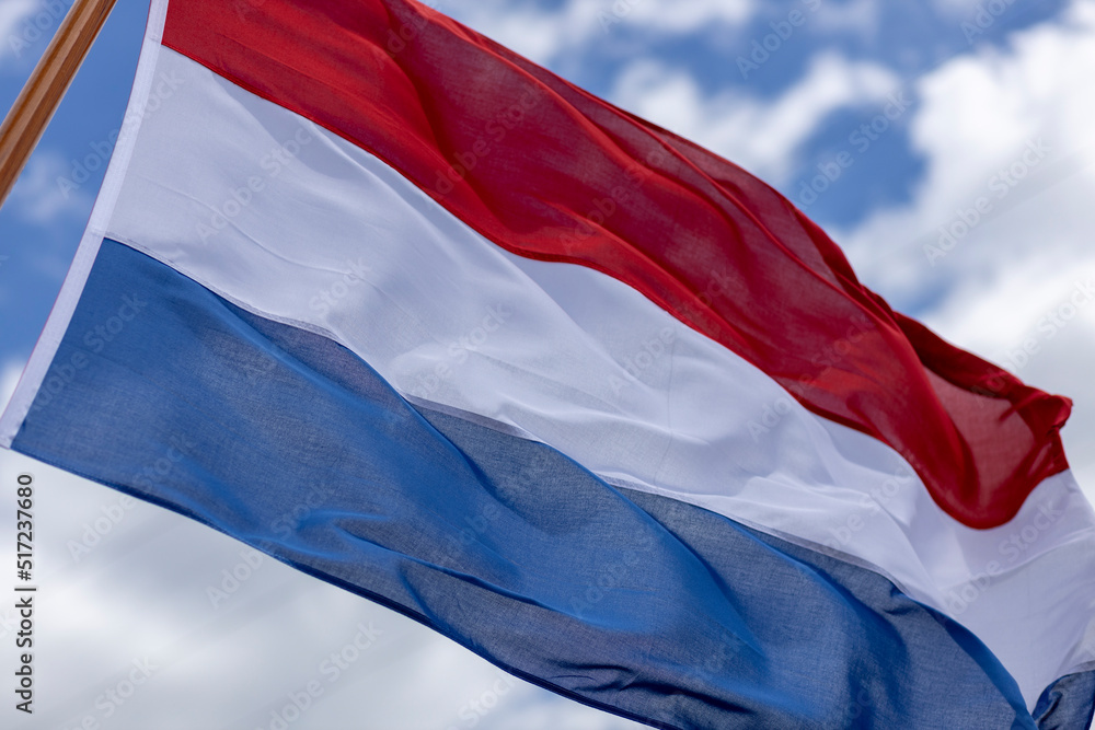 Naklejka premium Intrinsic folds in tricolor of Dutch national flag blowing in a strong wind with texture and detail against a blue sky with clouds