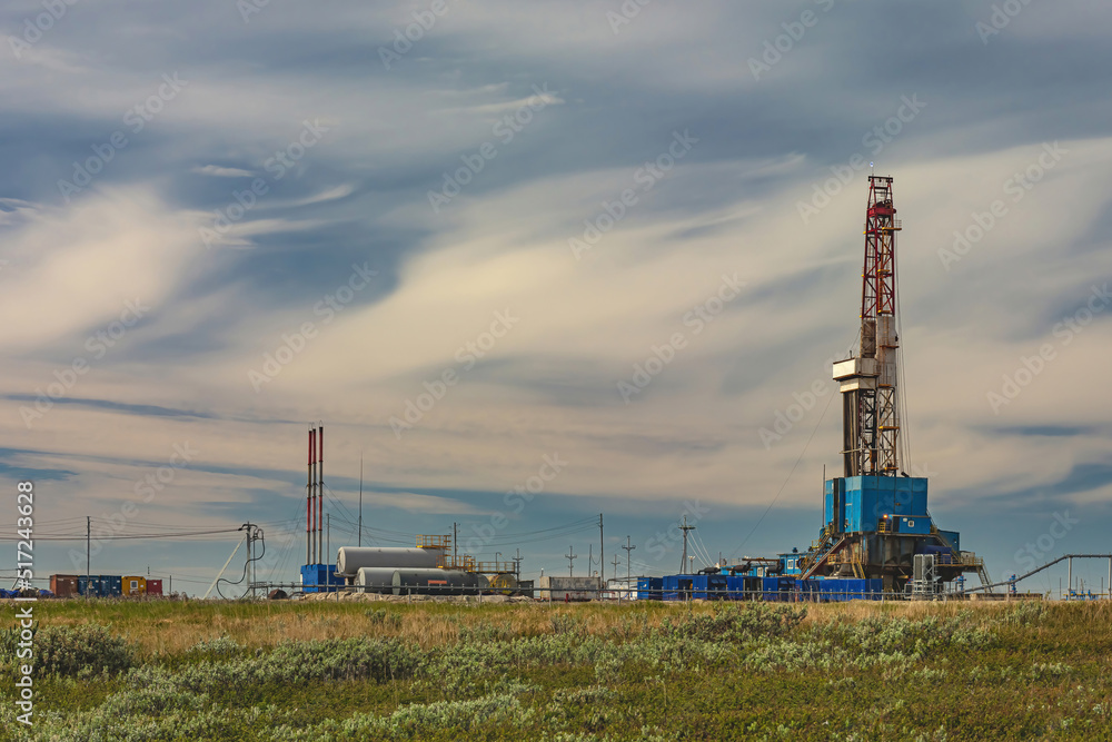 The spring landscape of the Arctic tundra against the background of infrastructure for drilling wells and oil and gas production. In the foreground is the sparse vegetation of the northern nature